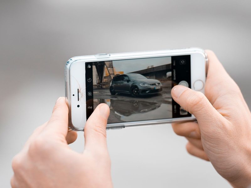 Hands framing a photo of a car on a phone camera
